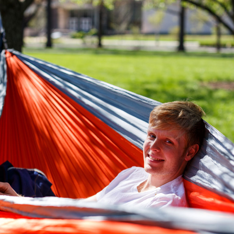 A student hanging out in a hammock on campus.